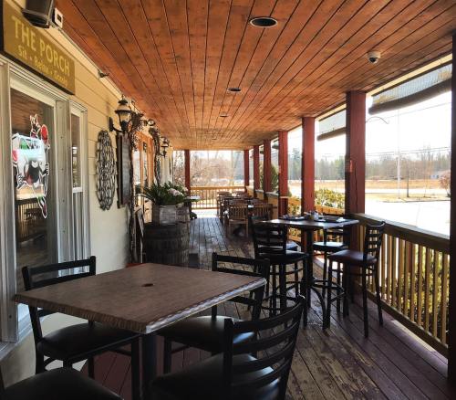 A cozy porch with wooden flooring, tables, and chairs, surrounded by plants and sunlight.