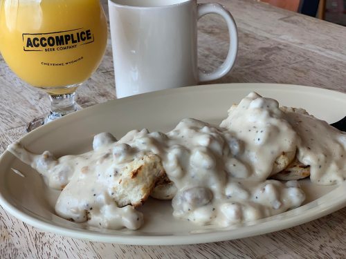 A plate of biscuits smothered in creamy sausage gravy, accompanied by a glass of orange juice and a white coffee mug.