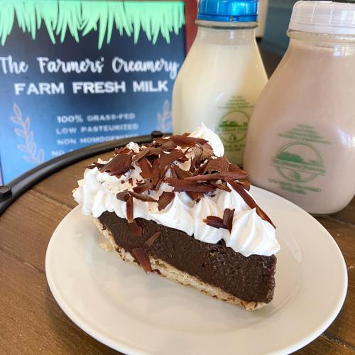A slice of chocolate cream pie topped with whipped cream and chocolate shavings, with two bottles of milk in the background.