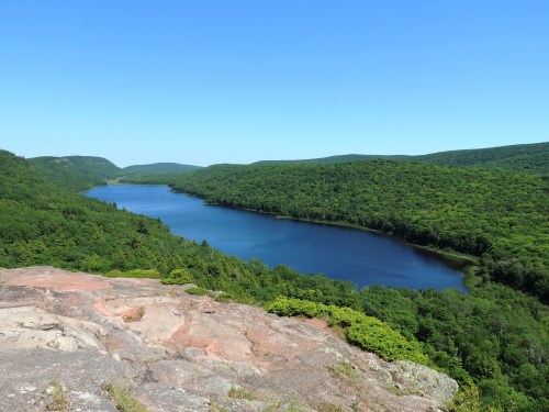 A serene view of a winding river surrounded by lush green hills under a clear blue sky.