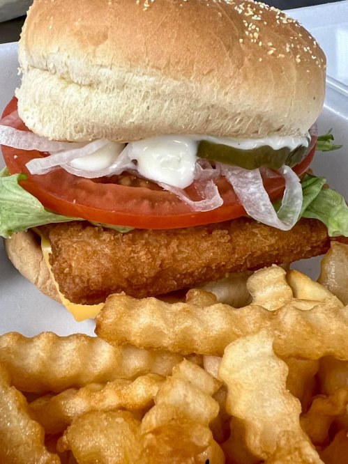 A crispy fish sandwich with lettuce, tomato, and pickles, served with crinkle-cut fries on the side.