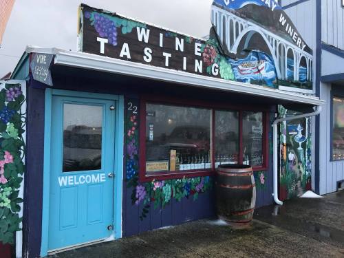 A colorful winery storefront with a "Wine Tasting" sign, blue door, and decorative grapevine murals.