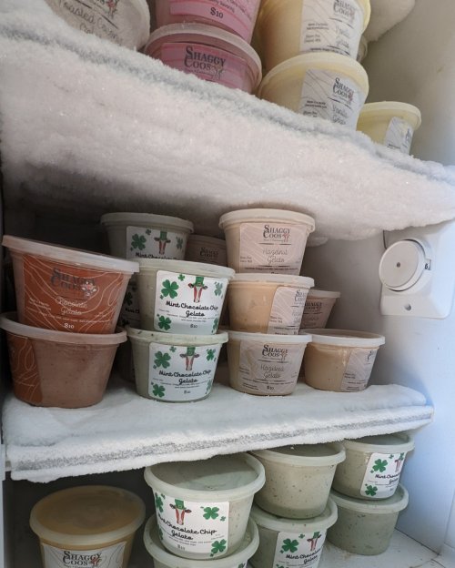 A freezer filled with various ice cream tubs stacked on shelves, some labeled with flavors and prices.