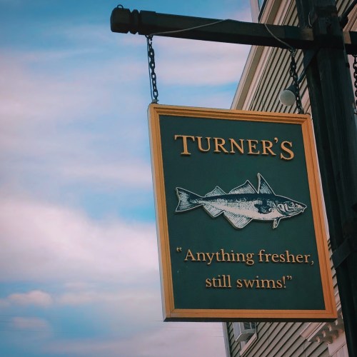 Sign for Turner's featuring a fish graphic and the slogan, "Anything fresher, still swims!" against a blue sky.