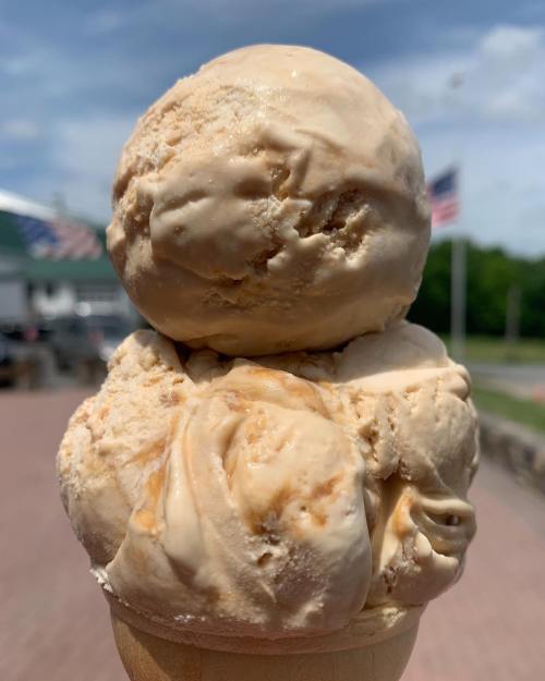 A close-up of a creamy ice cream cone with a scoop of caramel-flavored ice cream against a sunny outdoor background.