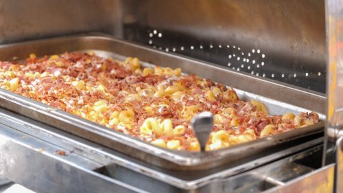 A tray of macaroni and cheese topped with crispy bacon bits, served in a stainless steel container.