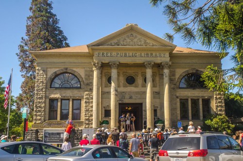 A historic public library building with people gathered outside, featuring columns and a large sign that reads "Free Public Library."