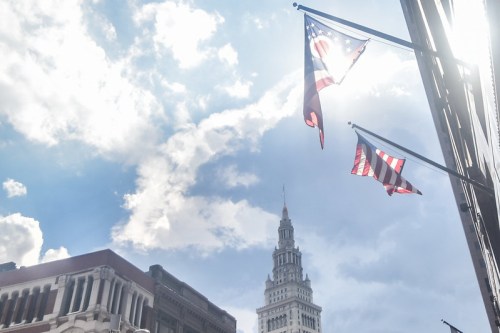 Two flags flutter against a bright sky, with a tall building visible in the background.