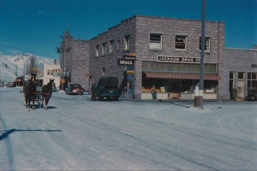 Historic street scene featuring Jackson Drug Co. building, snow-covered road, and vintage vehicles.
