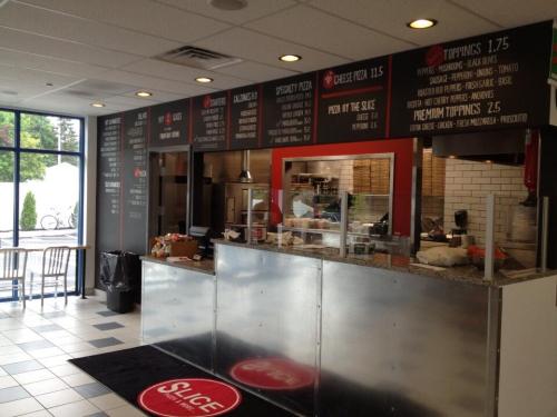 Interior of a pizza shop with a menu board, counter, and seating area. Clean, modern design with a welcoming atmosphere.
