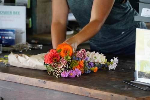 A person arranges a colorful bouquet of flowers on a wooden table, preparing it for sale.