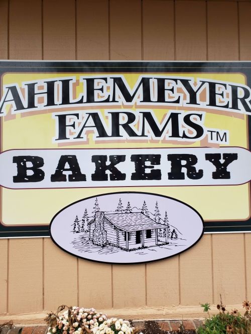 Sign for Ahlemeyer Farms Bakery featuring a rustic cabin illustration and a yellow background.