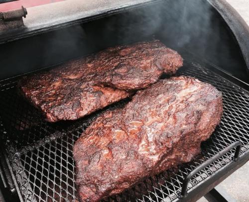 Two large, smoked briskets resting on a grill, surrounded by wisps of smoke.