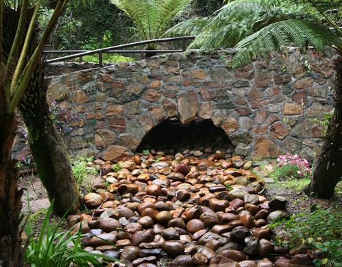 A stone archway surrounded by lush greenery and a bed of smooth, colorful pebbles in a serene garden setting.