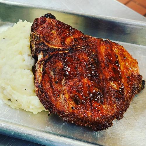A grilled pork chop served with creamy mashed potatoes on a metal tray.