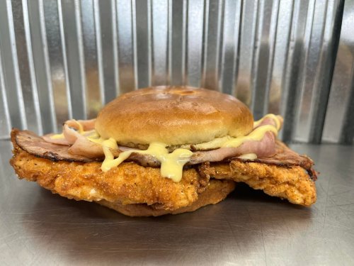 A close-up of a sandwich featuring a crispy chicken patty, ham, and a soft bun with a drizzle of sauce.