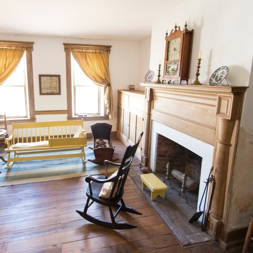 Cozy living room with a yellow rocking chair, wooden furniture, and a fireplace, featuring warm natural light.