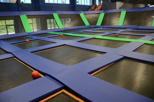 A spacious indoor trampoline park with blue and green trampolines and orange dodgeballs scattered across the area.