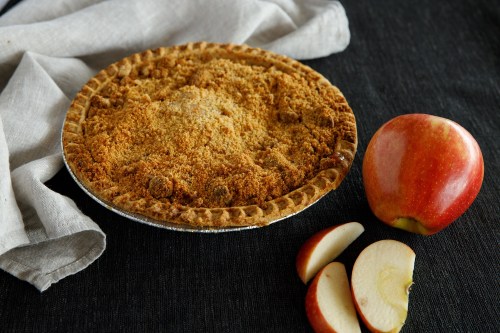 A freshly baked apple pie with a crumbly topping, accompanied by a whole red apple and sliced apple pieces.