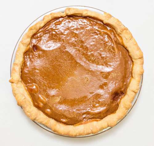 A freshly baked pumpkin pie in a glass pie dish with a golden-brown crust.