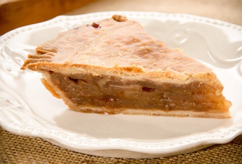 A slice of apple pie on a decorative white plate, showcasing a golden crust and apple filling.