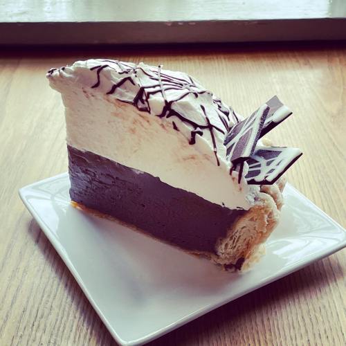 A slice of layered chocolate and cream cake topped with chocolate drizzle, served on a white plate.