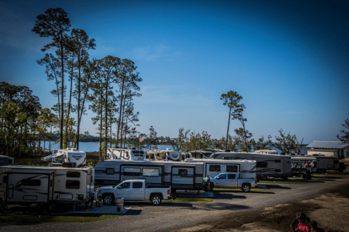 A scenic RV park with several campers and trees, set against a clear blue sky and a lake in the background.