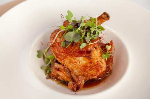 A beautifully plated fried chicken piece garnished with microgreens and red saffron strands on a white dish.