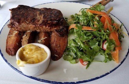 A plate featuring grilled steak, fried plantains, and a fresh salad with mixed greens and colorful vegetables.