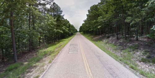 A straight, empty road lined with trees on both sides, leading into the distance.