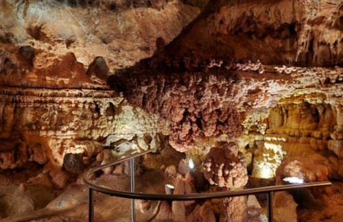 A cave interior featuring unique rock formations and illuminated stalactites, with a railing for visitors.