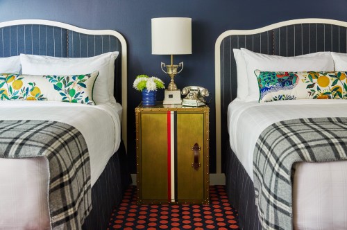 A cozy bedroom with two beds, colorful pillows, a lamp, and a decorative nightstand with flowers and a vintage phone.