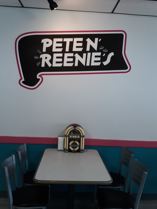 A diner table with a jukebox in front of a wall sign that reads "PETE N' REENIE'S."