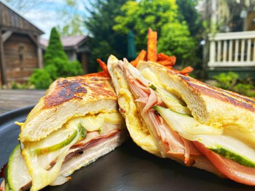 A close-up of a grilled sandwich filled with ham, cheese, and vegetables, served with crispy fries on a black plate.
