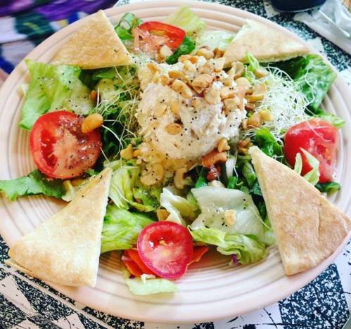 A colorful salad with lettuce, tomatoes, sprouts, and a mound of nuts, served with triangular pita bread.