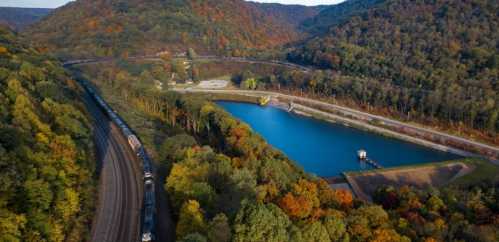 Aerial view of a train along a winding track near a serene blue lake surrounded by colorful autumn foliage.