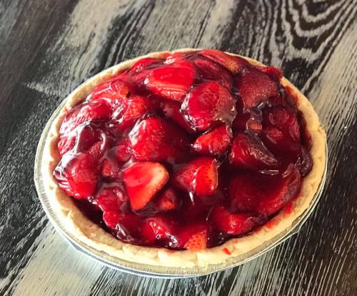A fresh strawberry pie topped with glossy red glaze, sitting in a silver pie dish on a dark wooden surface.