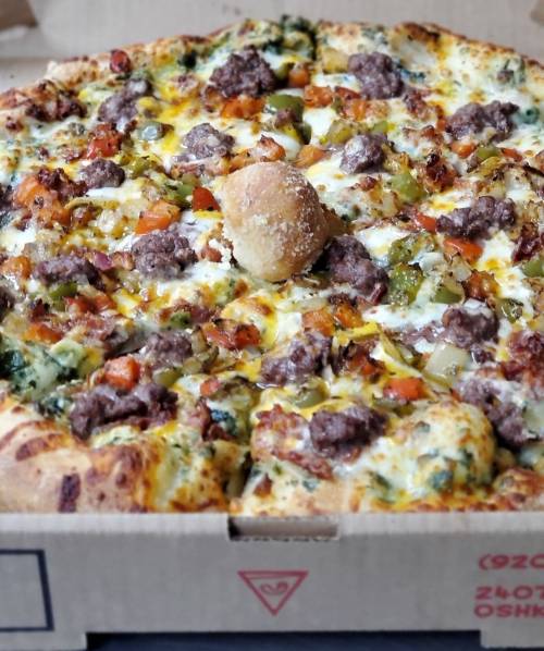 A close-up of a pizza topped with ground beef, vegetables, and a breadball, in a pizza box.