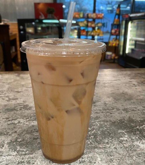 A tall iced coffee drink with layers of cream and coffee, served in a clear cup with a straw on a textured surface.