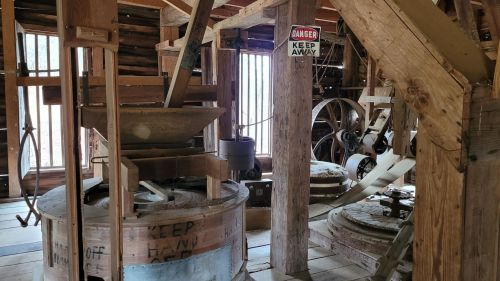 Interior of an old mill with wooden machinery, grain grinders, and a "Danger: Keep Away" sign on the wall.