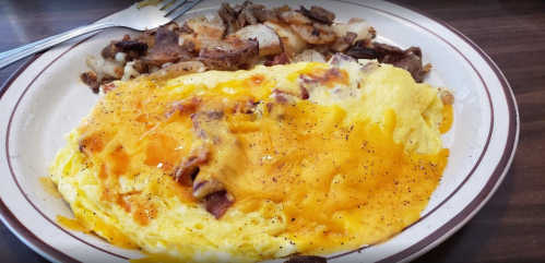 A plate of fluffy cheese omelette with crispy hash browns on the side, garnished with black pepper.