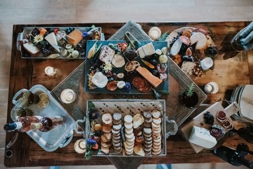 A beautifully arranged charcuterie board with various cheeses, meats, fruits, and decorative flowers on a wooden table.