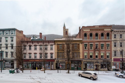 Historic buildings line a snowy street, with a church steeple visible in the background under a cloudy sky.