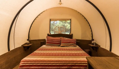 Cozy interior of a glamping tent featuring a bed with striped bedding and wooden accents.