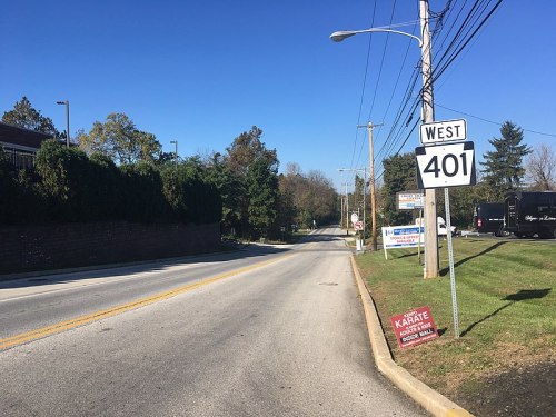 A view of a road labeled "West 401," with signs for karate and other businesses along the side. Trees line the background.