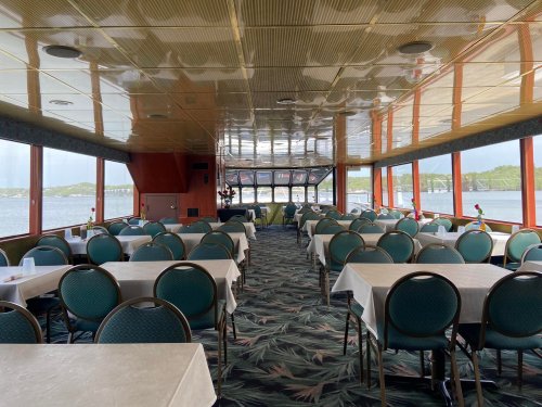 Interior of a dining area with tables and chairs, large windows overlooking water, and a scenic view outside.