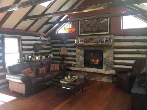 Cozy log cabin living room with a stone fireplace, leather sofas, and wooden beams. Warm and inviting atmosphere.