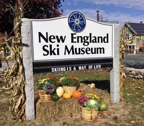 Sign for the New England Ski Museum, featuring colorful pumpkins and flowers in front, with autumn decorations.