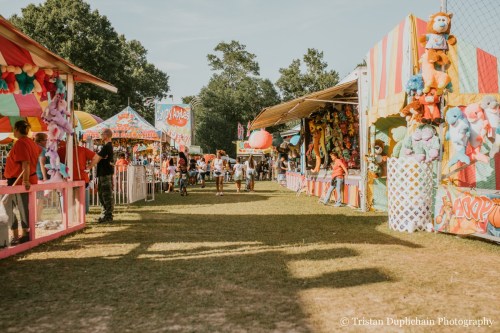 A vibrant carnival scene with colorful booths, games, and people enjoying the festivities on a sunny day.