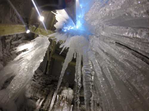 Icicles hang from a ceiling, illuminated by blue light, creating a shimmering, icy landscape.